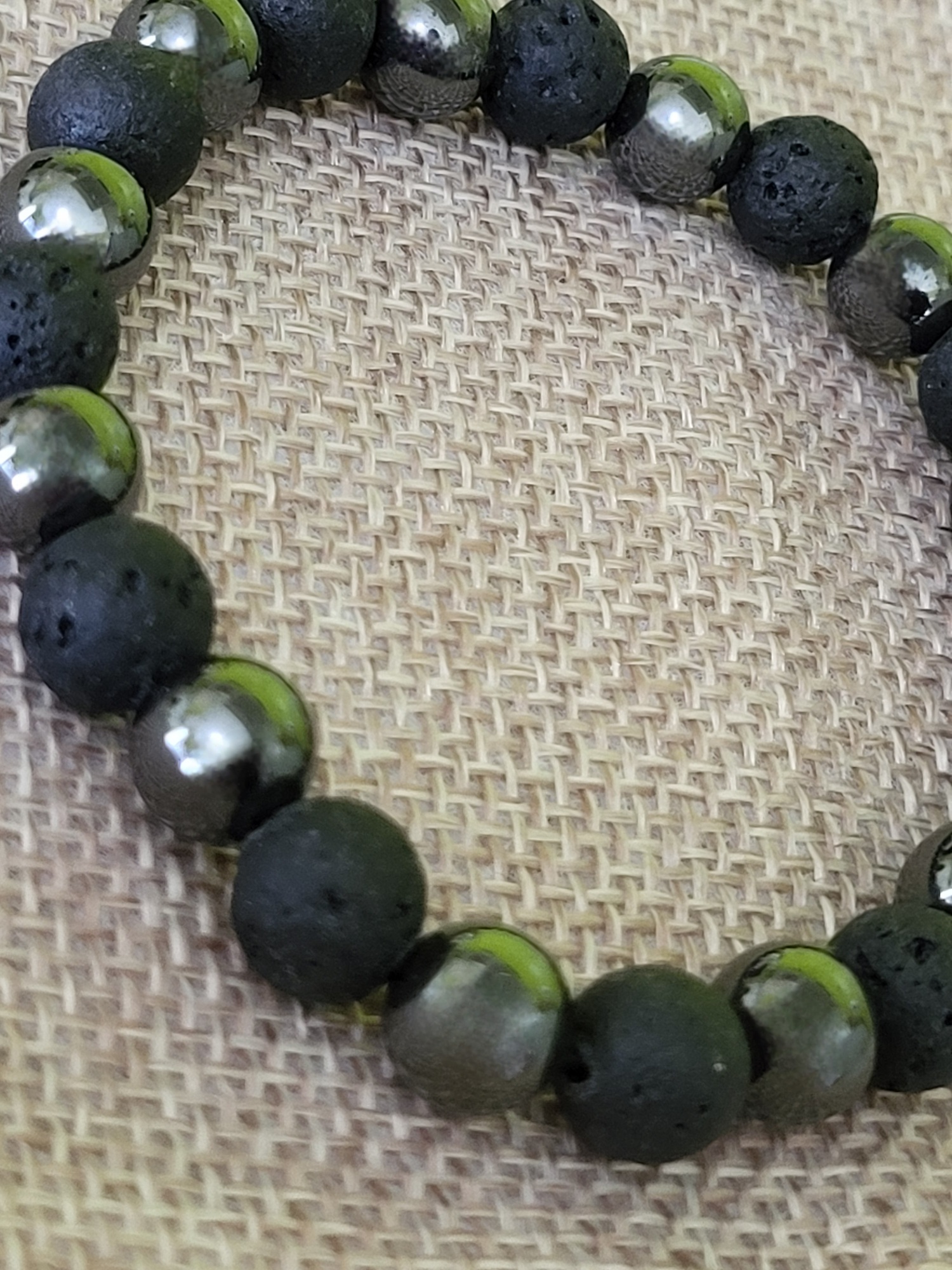 Détail des perles du bracelet Intensité Full Black : pierre de lave noire et perles d'hématite grise sur un support en toile de jute.