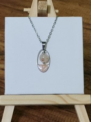 Collier fantaisie artisanal nommé "Goutte de Citrine". Le pendentif présente une perle ronde en citrine véritable (obtenue par améthyste chauffée) suspendue dans un cadre ovale argenté. La base du pendentif est ornée d'une finition scintillante rosée. Bijou élégant et lumineux pour femme par Perle et Coquette.